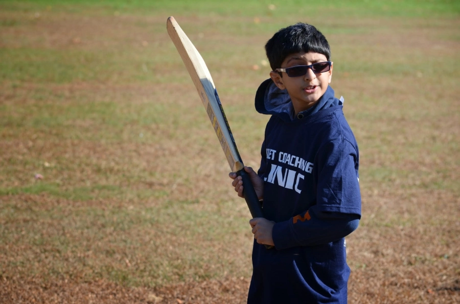 Young cricket player practicing batting at a coaching clinic, holding a bat with proper stance on a field
