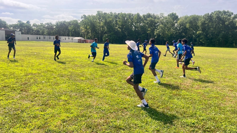 A group of young athletes in blue CricMax uniforms running on a grassy field as part of their cricket fitness and conditioning program.