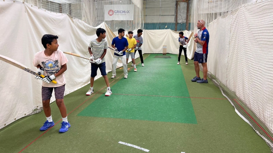 A group of young cricketers practicing batting techniques under the guidance of a coach at CricMax’s indoor training facility, focusing on stance and swing control.