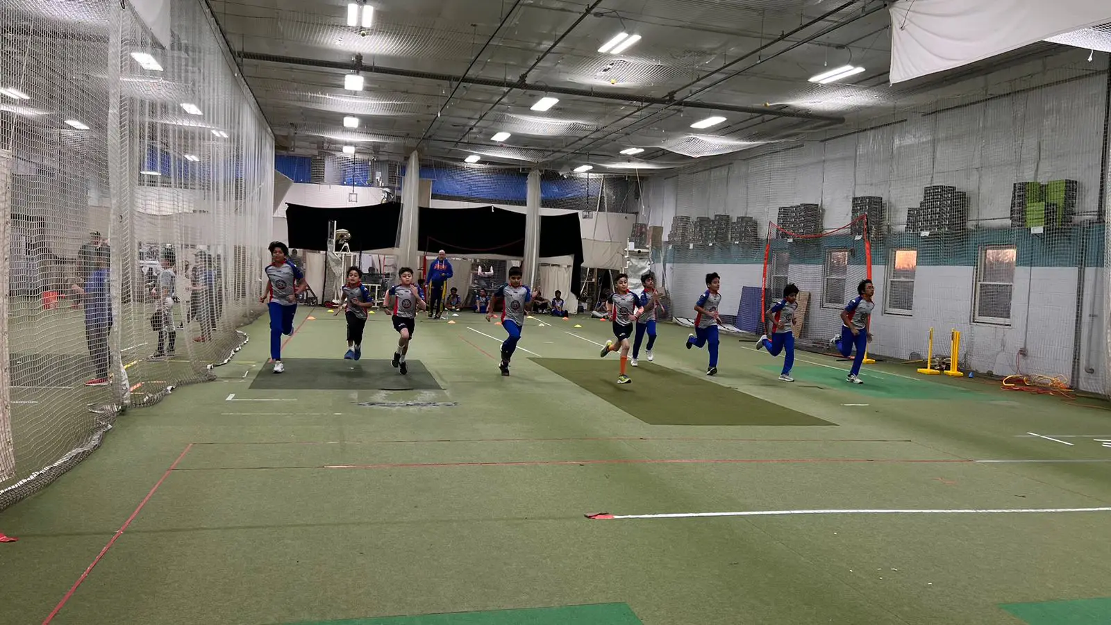 Young cricket players sprint indoors during a fitness drill at a training facility. The activity highlights the sport’s emphasis on agility, endurance, and full-body movement as part of cricket training for children.
