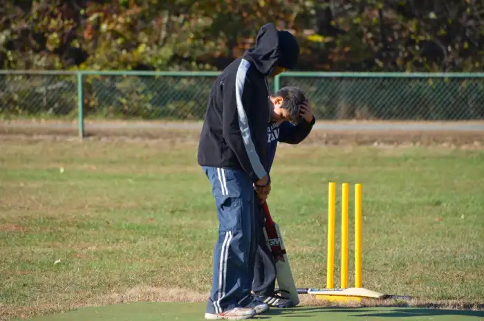 A cricket coach gently guiding a young player who appears overwhelmed during practice. The child holds their head while receiving one-on-one support, reflecting emotional pressure, reassurance, and the importance of positive coaching in youth cricket.